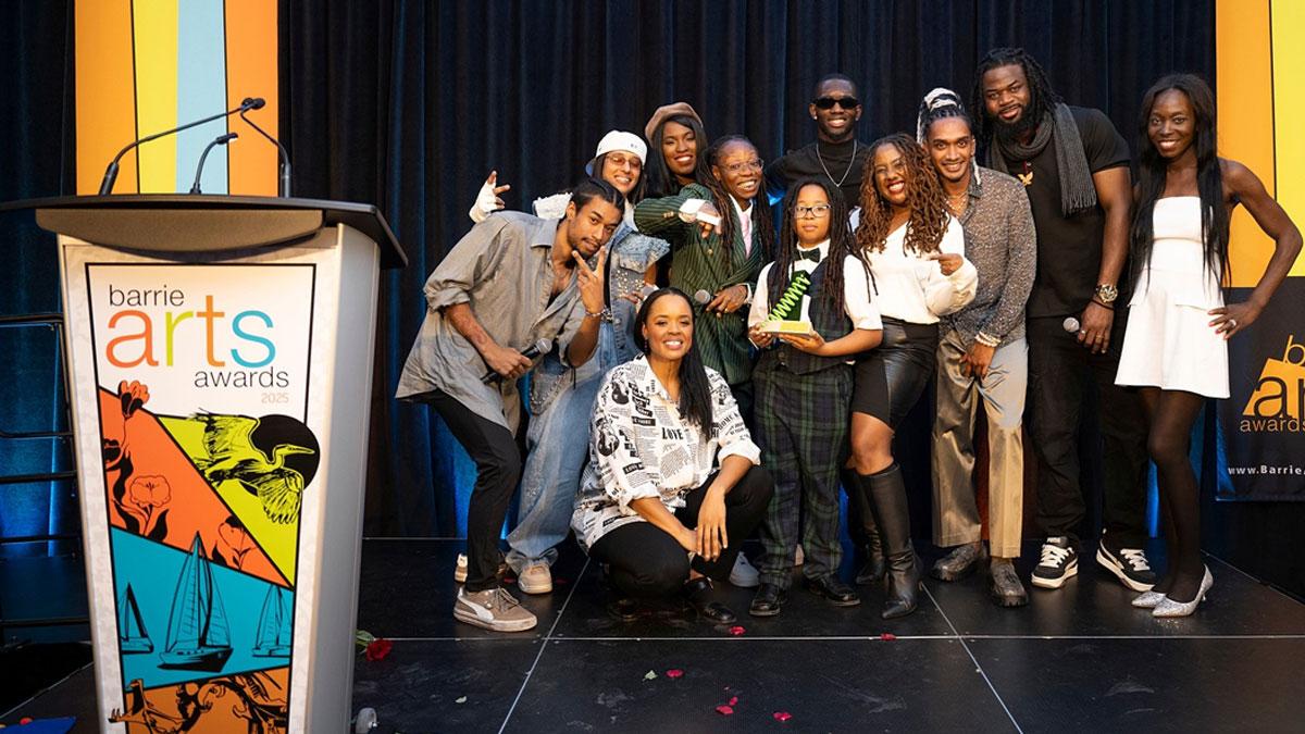A group of people standing on the Barrie Arts Awards stage. The person in the middle is holding an award.