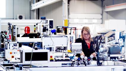 Manufacturing assembly line. There is a woman technician working on the background.
