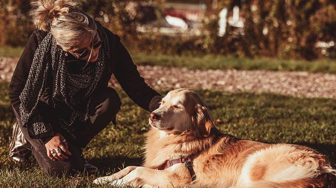 Ariadna crouched down outside, petting dog laying on grass