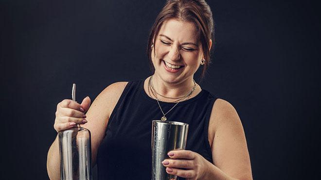 Jenna smiling with eyes closed, holding cocktail mixer, black background