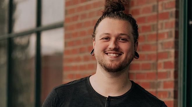 Headshot of Kyle smiling at camera, brick building in background