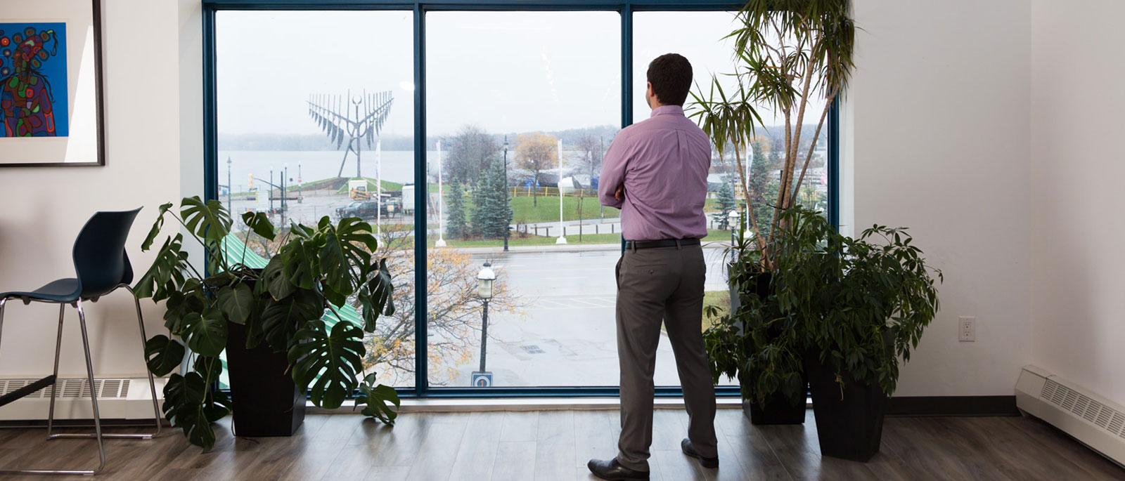 Person standing in front of window with arms crossed. The subject is looking out through the window.